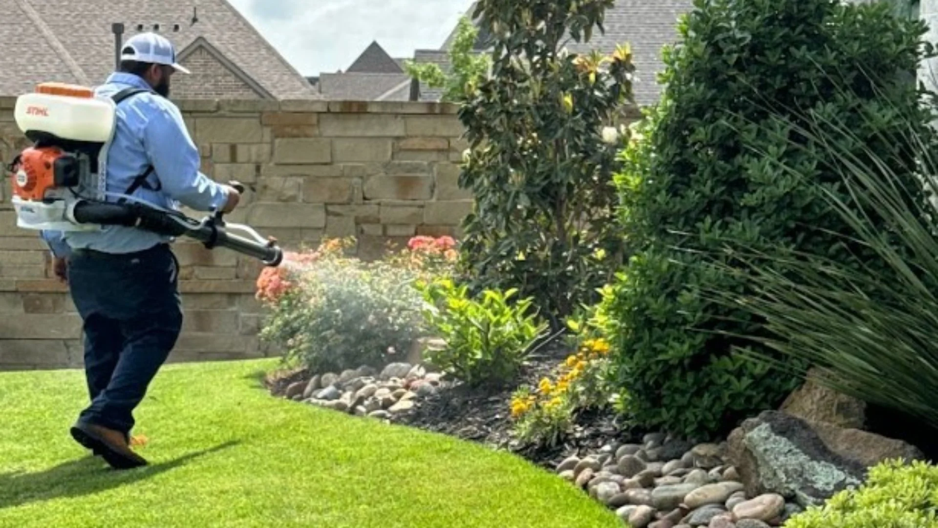 Worker applying pest control treatment in landscape bed