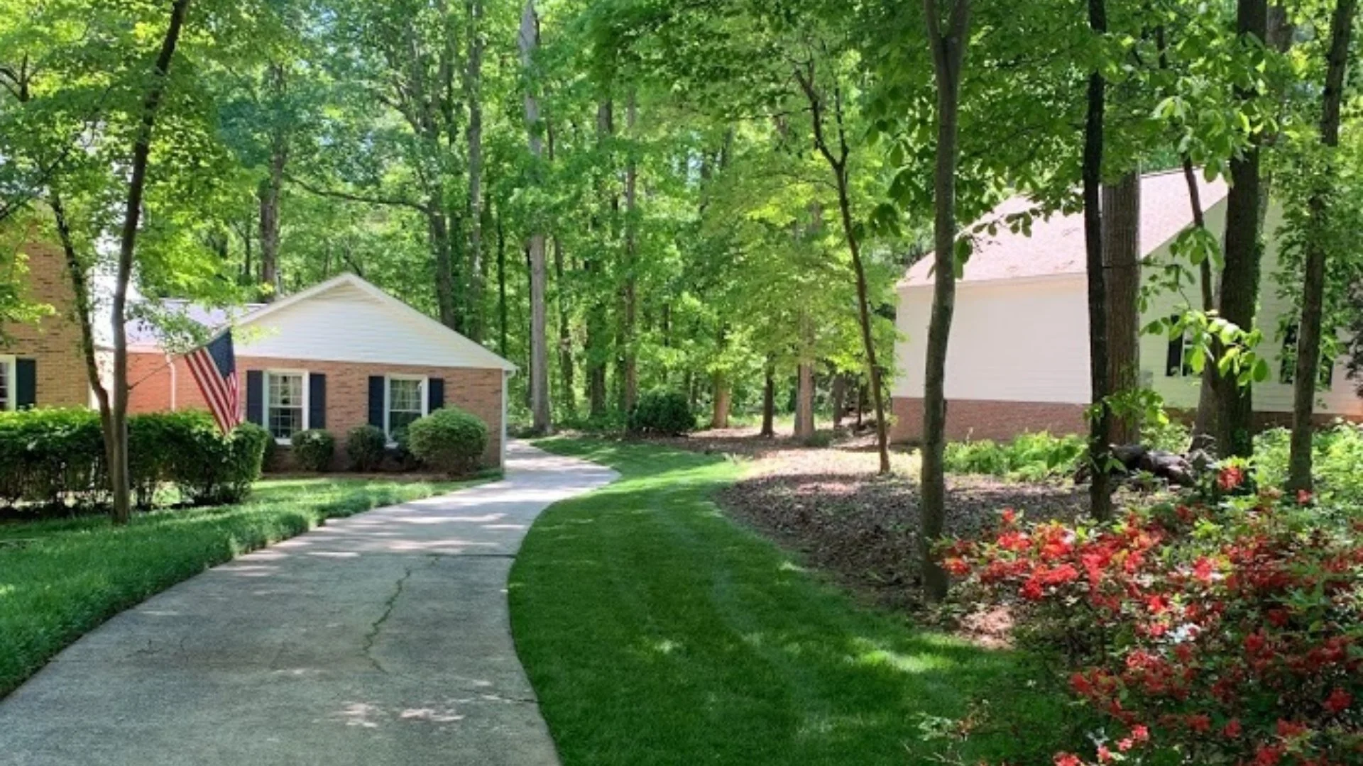 House in Dallas, TX surrounded by trees, lawn, shrubs, and flowers.