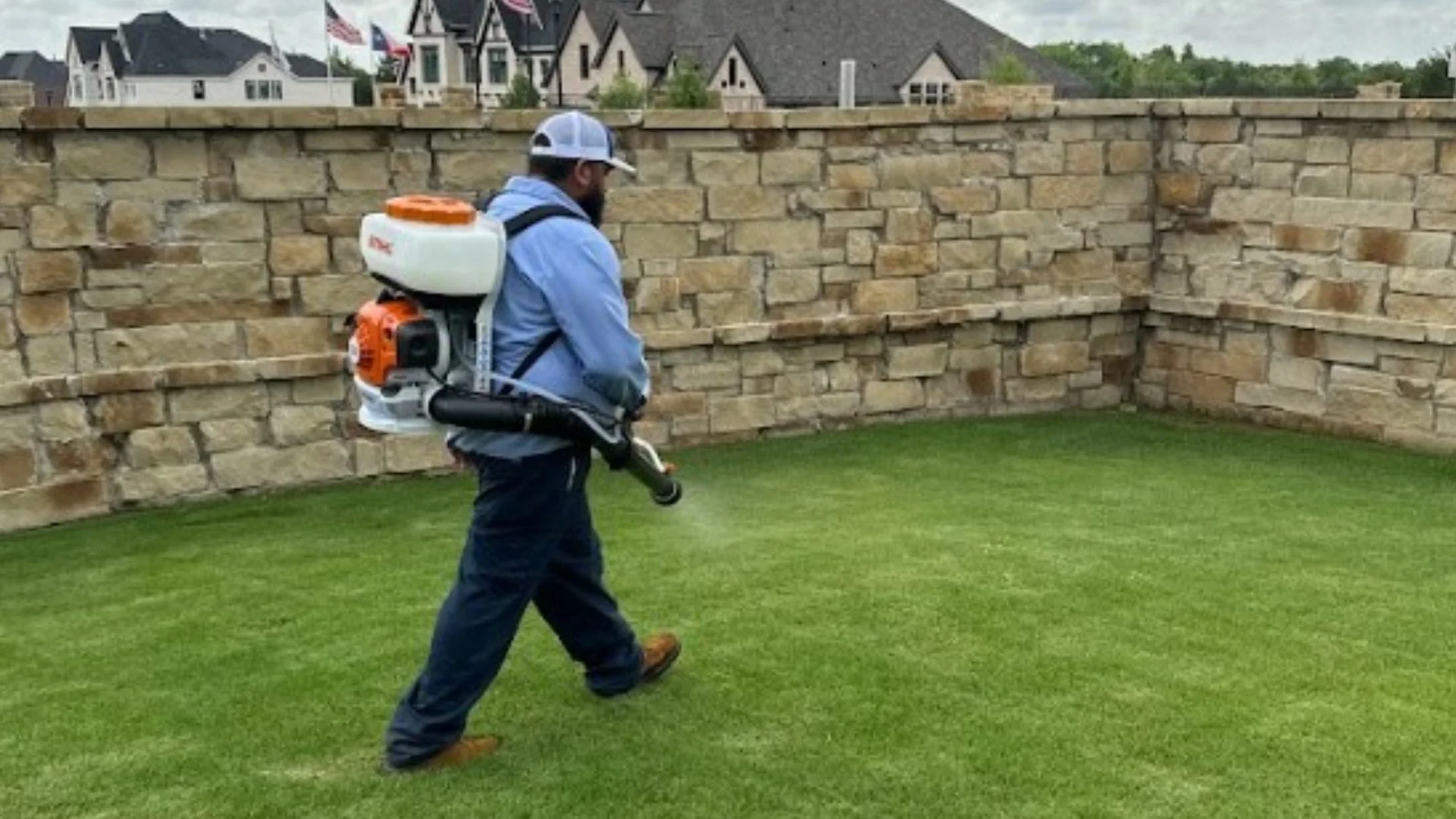 Technician applying pest control next to rock wall in Grand Prairie, TX.