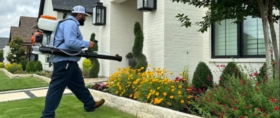 Worker in Arlington, TX, applying pest control to a landscape bed.