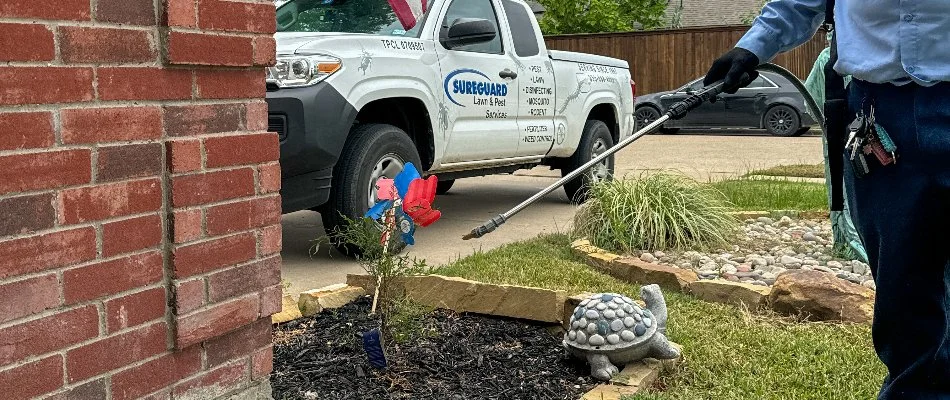 Worker spraying a perimeter pest control treatment to the side of a home in Dallas, TX.