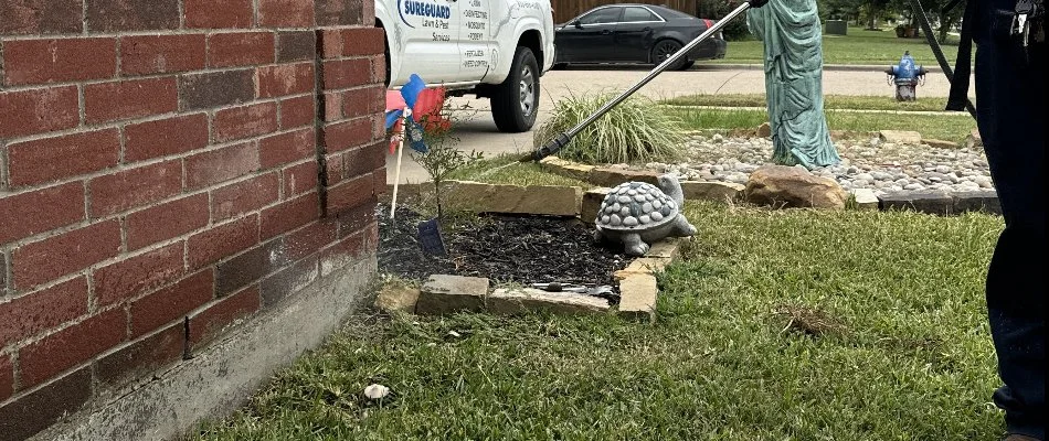 A worker spraying a pest treatment to a brick house in McGregor, TX.