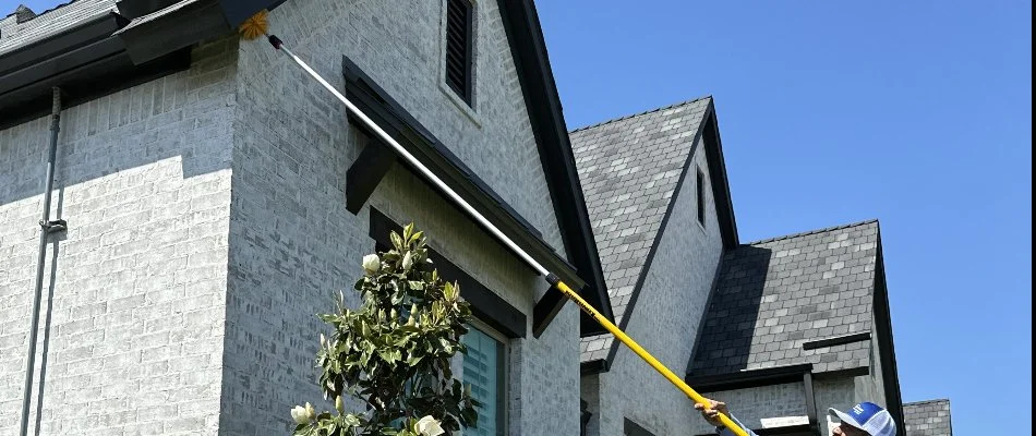 A worker using a pest brusher to dust a house's eaves in McKinney, TX.